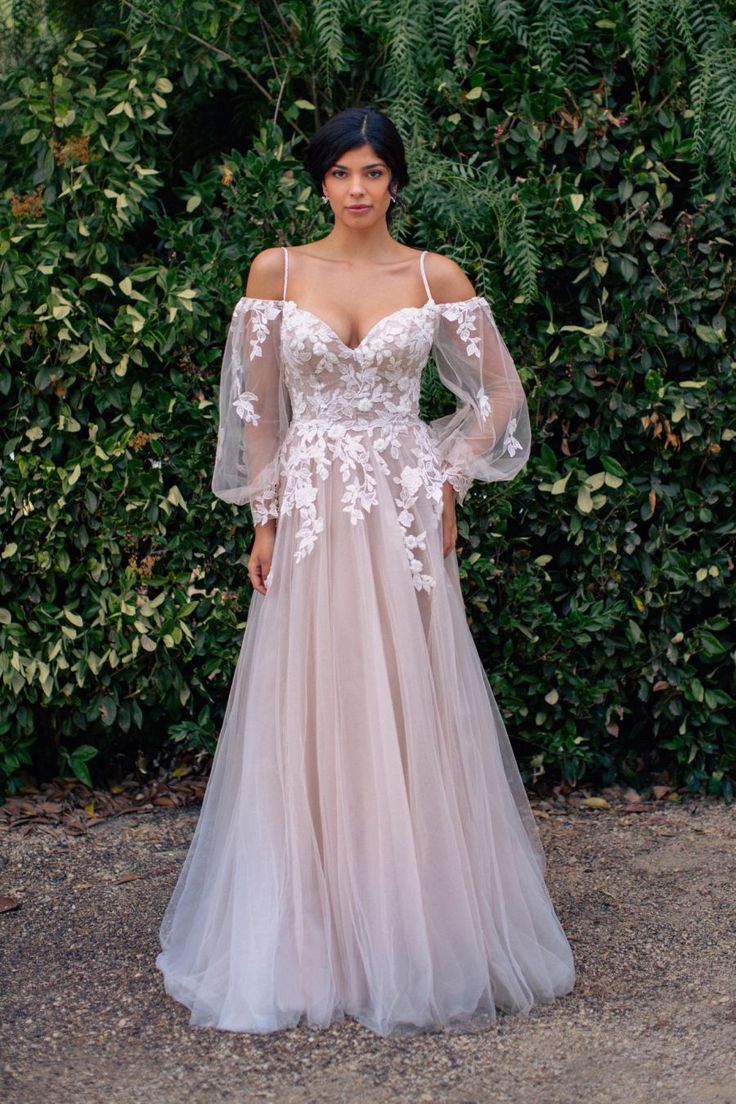 a woman standing in front of a bush wearing a dress with long sleeves and flowers on it