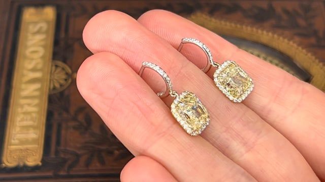 This wonderful pair of pierced earrings feature an 18K yellow gold dangle style halo setting and topped with a platinum half hoop. Each earring is accented with one (1) cushion modified brilliant cut fancy yellow colored diamond surrounded by a halo of twenty-six (26) round diamonds all prong set. The top of each earring has a half hoop containing thirteen (13) diamonds set outside and inside of the hoop and all bead set. The earrings are finished with a post and la pousette backs. The earring measure 22.7mm from top to bottom of dangle and have a width of 9.51mm. Luxury Yellow Gold Earrings With Halo Design, Yellow Halo Design Earrings In Fine Jewelry, Fine Jewelry Yellow Earrings With Halo Design, Yellow Halo Design Fine Jewelry Earrings, Yellow Halo Design Earrings Fine Jewelry, Luxury Platinum Diamond Earrings With Halo Design, Luxury Diamond Dangle Earrings With Halo Design, Luxury Gia Certified Yellow Gold Diamond Earrings, Luxury Dangle Diamond Earrings With Halo Design