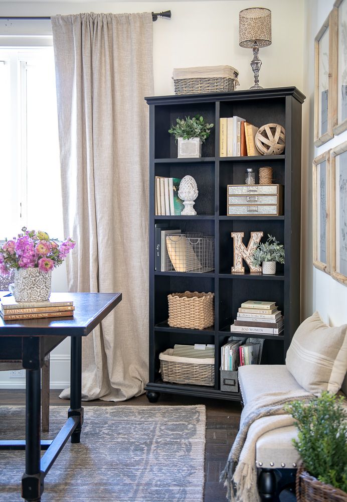 a living room filled with furniture and bookshelves next to a window covered in curtains