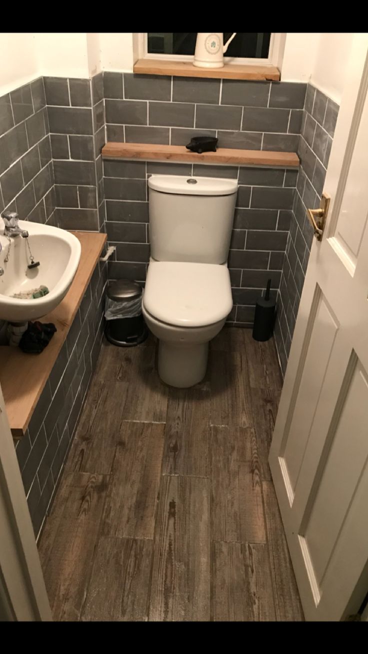 a toilet and sink in a bathroom with grey tiles on the walls, wood flooring