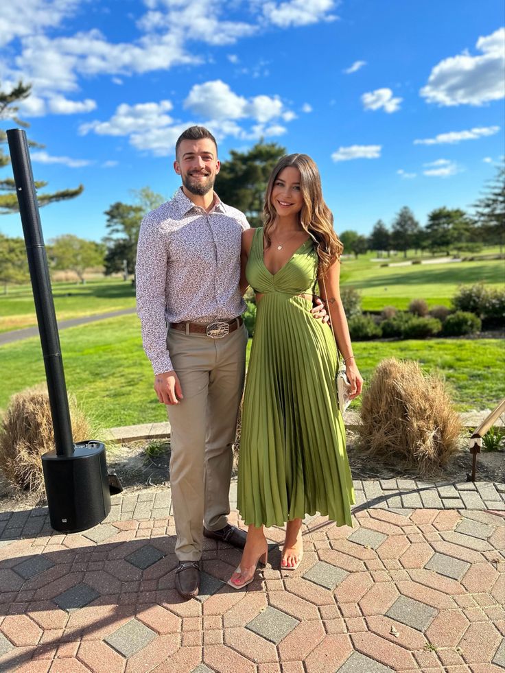 a man and woman standing next to each other in front of a green field with trees