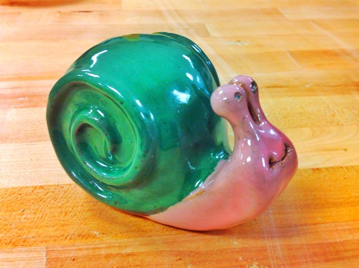 a green and pink snail sitting on top of a wooden table