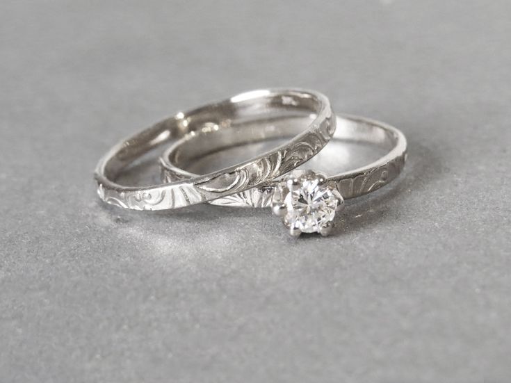 two silver wedding rings sitting next to each other on top of a gray tablecloth