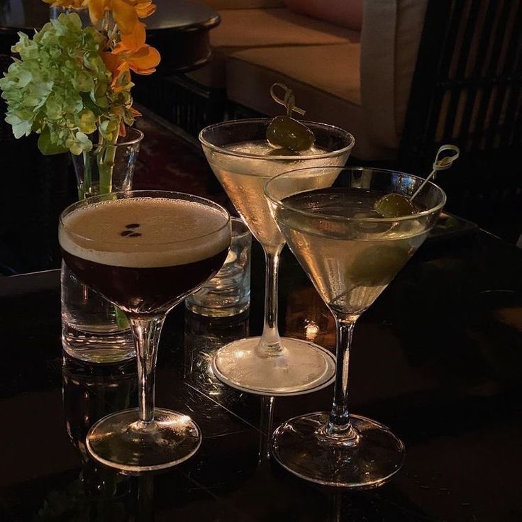 three martini glasses sitting on top of a table next to a vase filled with flowers