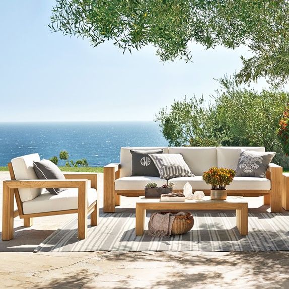 an outdoor furniture set on a patio near the ocean with trees and water in the background