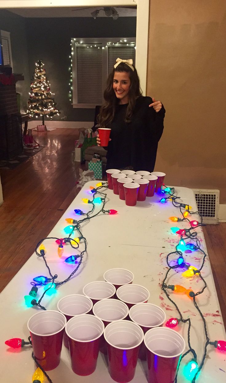 a woman standing in front of a table with cups on it and christmas lights strung across the table