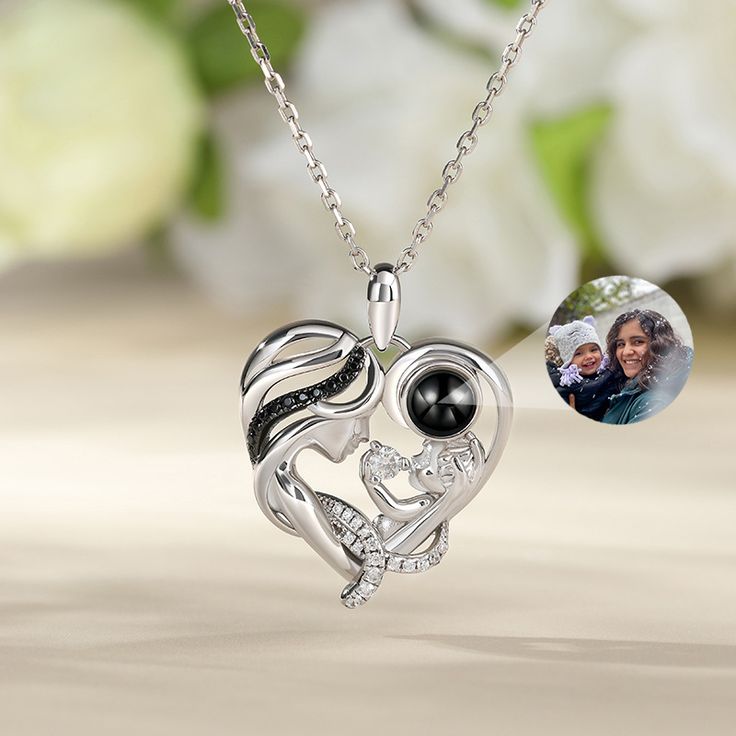 This is a mysterious necklace, personalized for the moment you love most on a projection necklace! Crafted in sterling silver, this endearing necklace representing a mother holding her child features a heart-shaped frame with a dangling projection stone and smaller stones embellishing the mother’s curvy hair. The baby is naughtily playing and the mother looks at her child patiently with love. The beautiful lines embody the gentle, graceful mother’s love. She always protects her naughty and innoc Mother's Day Gift Birthstone Necklace, Silver Keepsake Necklaces For Mother's Day, Silver Keepsake Necklace For Mother's Day, Silver Necklace Keepsake For Mother's Day, Mother's Day Keepsake Silver Necklace, Customizable Black Necklaces For Mother's Day, Mother's Day White Gold Pendant Birthstone Necklace, White Gold Pendant Birthstone Necklace For Mother's Day, Elegant Silver Birthstone Necklace As Gift For Mom