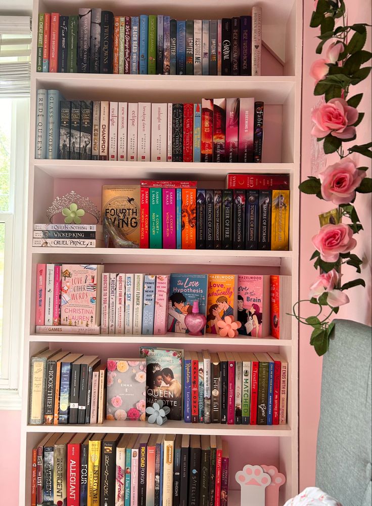 a book shelf filled with lots of books next to a vase full of pink roses