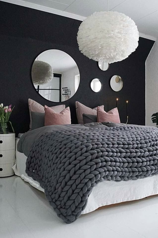 a large bed sitting under a round mirror next to a white vase filled with flowers