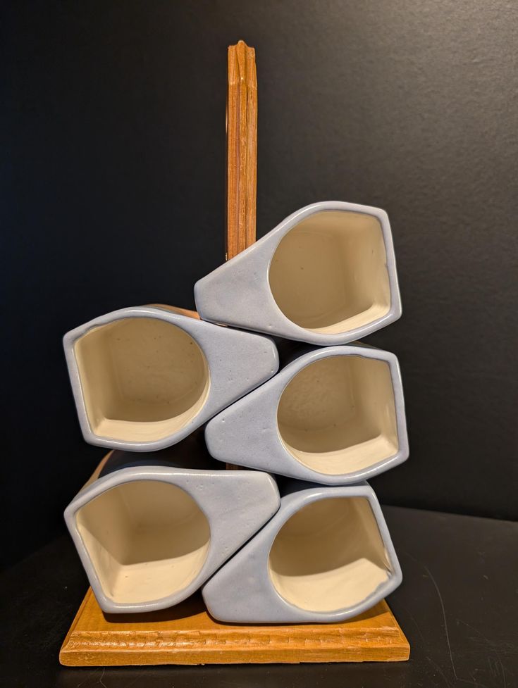 four white vases stacked on top of each other in front of a black wall