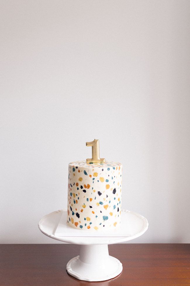 a white cake with gold top sitting on a wooden table in front of a white wall