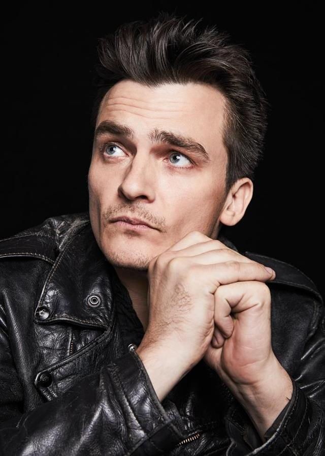 a man in a black leather jacket is looking at the camera with his hand on his chin