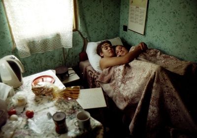 two people laying in a bed next to each other with dishes on the table and coffee mugs