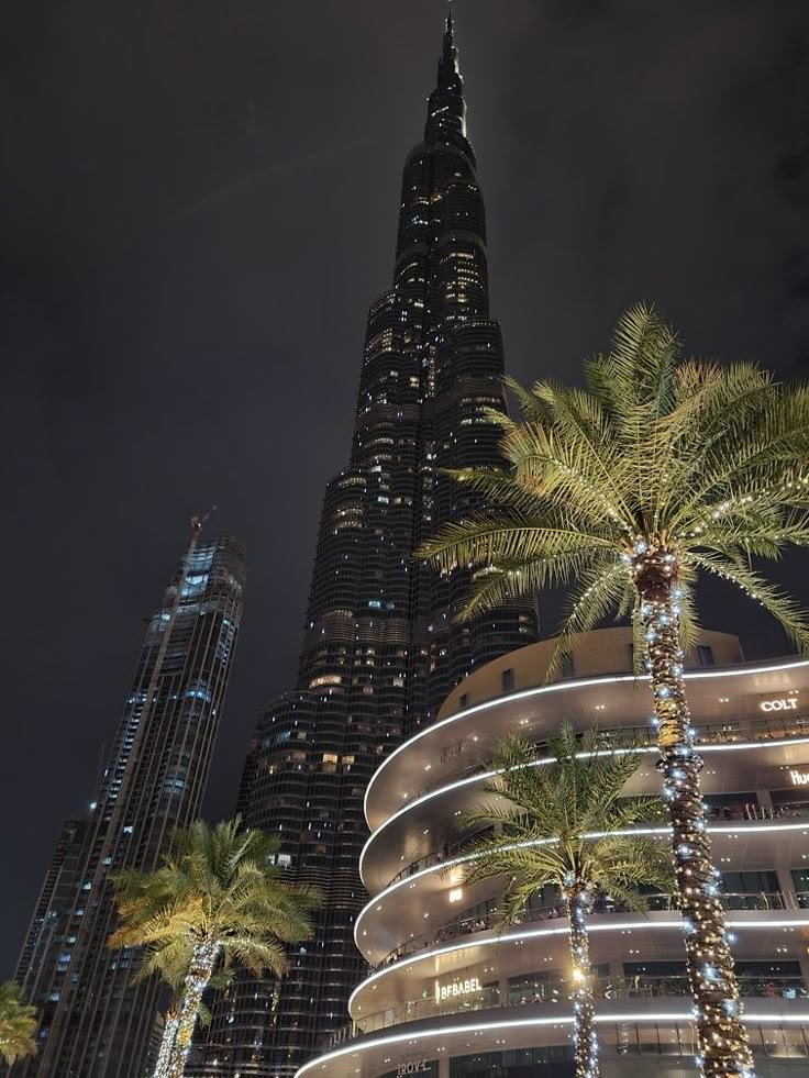 the burj building is lit up at night with palm trees in front of it