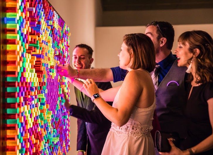 a group of people standing next to each other in front of a wall covered with colorful lights