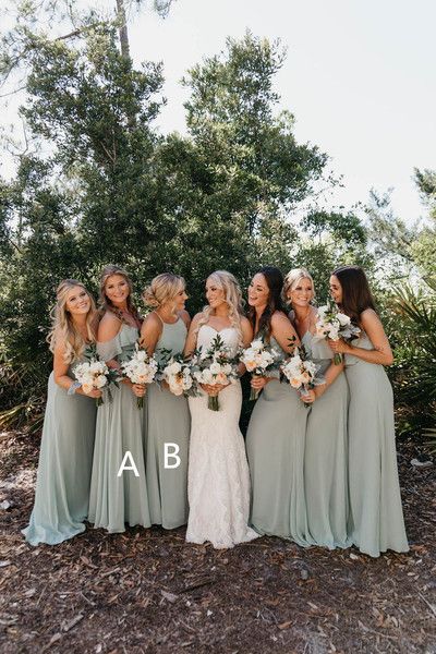 a group of women standing next to each other in front of trees and bushes holding bouquets