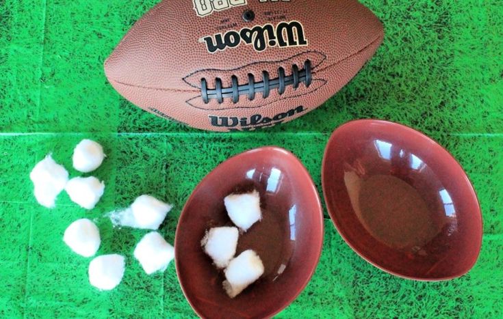 two bowls filled with marshmallows next to a football on a green surface