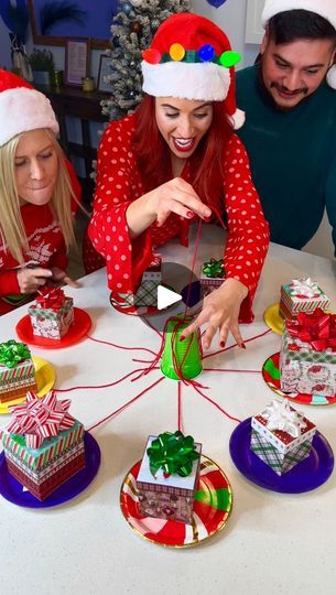 three people in santa hats around a table with presents