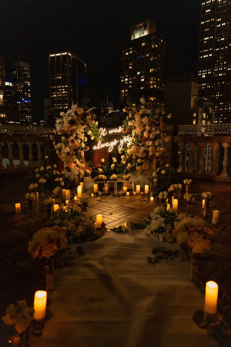 an outdoor wedding setup with candles and flowers on the ground in front of skyscrapers