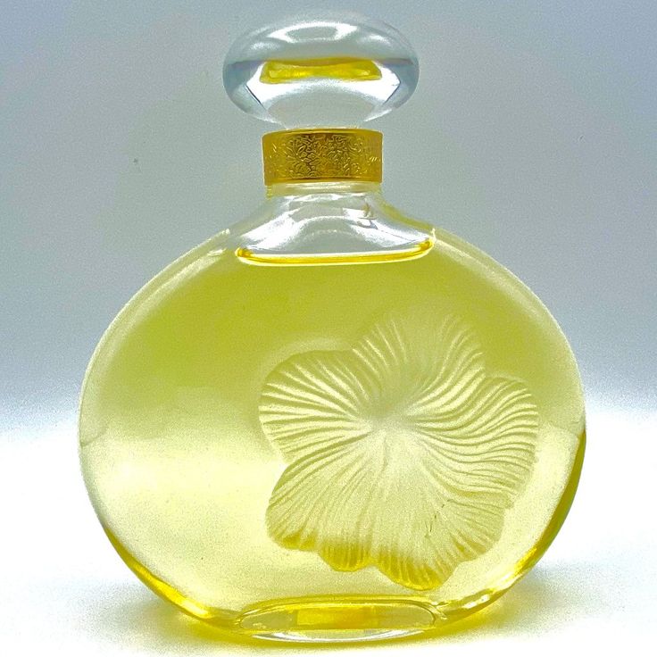 a yellow glass bottle with a flower etched on the top and bottom, in front of a white background