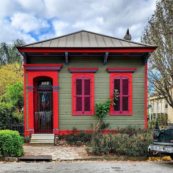 a green house with red shutters and a black truck parked in front of it