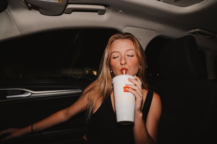 a woman sitting in the back seat of a car drinking from a cup