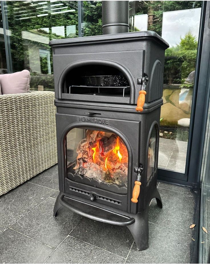 a black stove with flames in it sitting on a patio next to a wicker chair