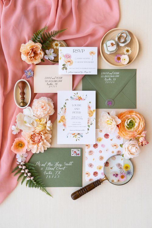 the wedding stationery is laid out on top of pink fabric and flowers, including an envelope