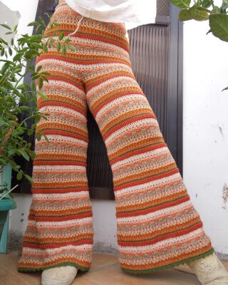 a woman is standing in front of a potted plant with her legs crossed and wearing crochet pants