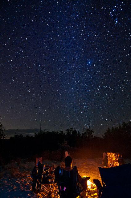 two people sitting around a campfire under the stars