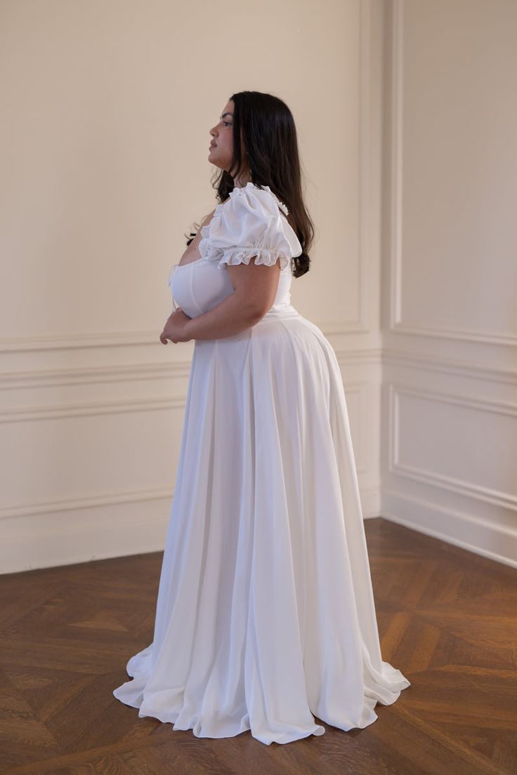 a woman in a white dress is standing on the floor and looking off into the distance