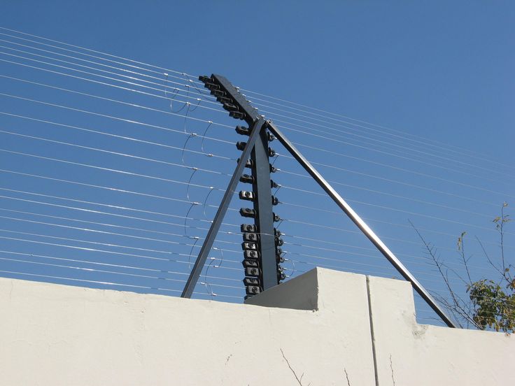 a tall metal object sitting on top of a white wall next to a building with wires above it