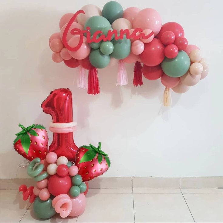 a number one balloon with strawberries and balloons attached to the wall in front of it