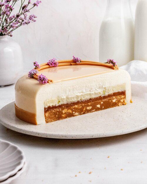 a piece of cake sitting on top of a white plate next to a vase with purple flowers