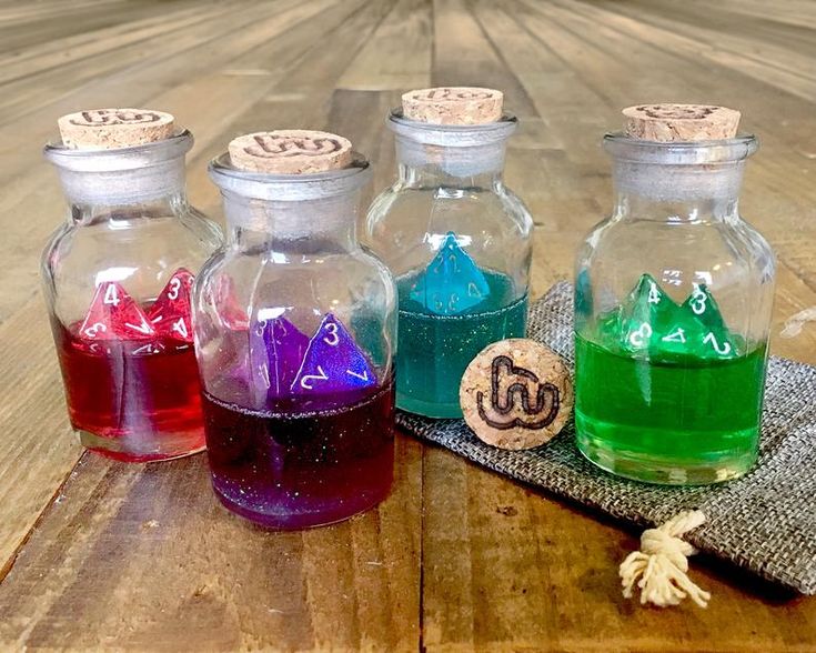 four glass bottles filled with different colored liquids on top of a wooden table next to a cloth