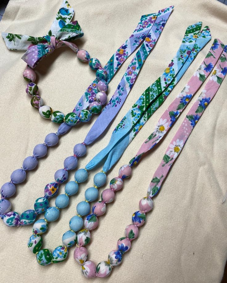 four different necklaces are laid out on a table top, one is blue and the other has pink beads