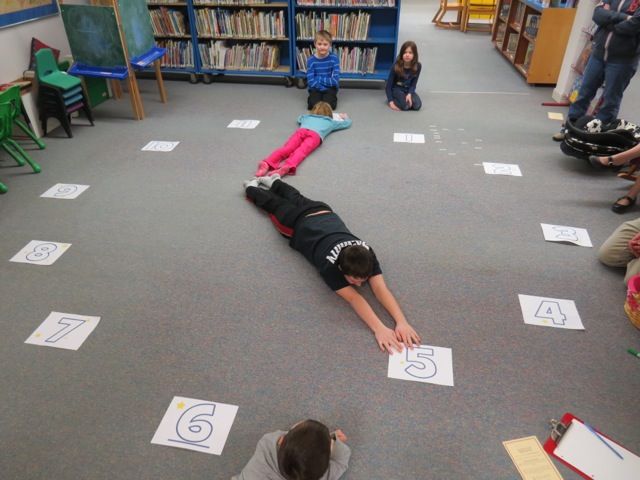 a group of children sitting on the floor in front of bookshelves with numbers written on them