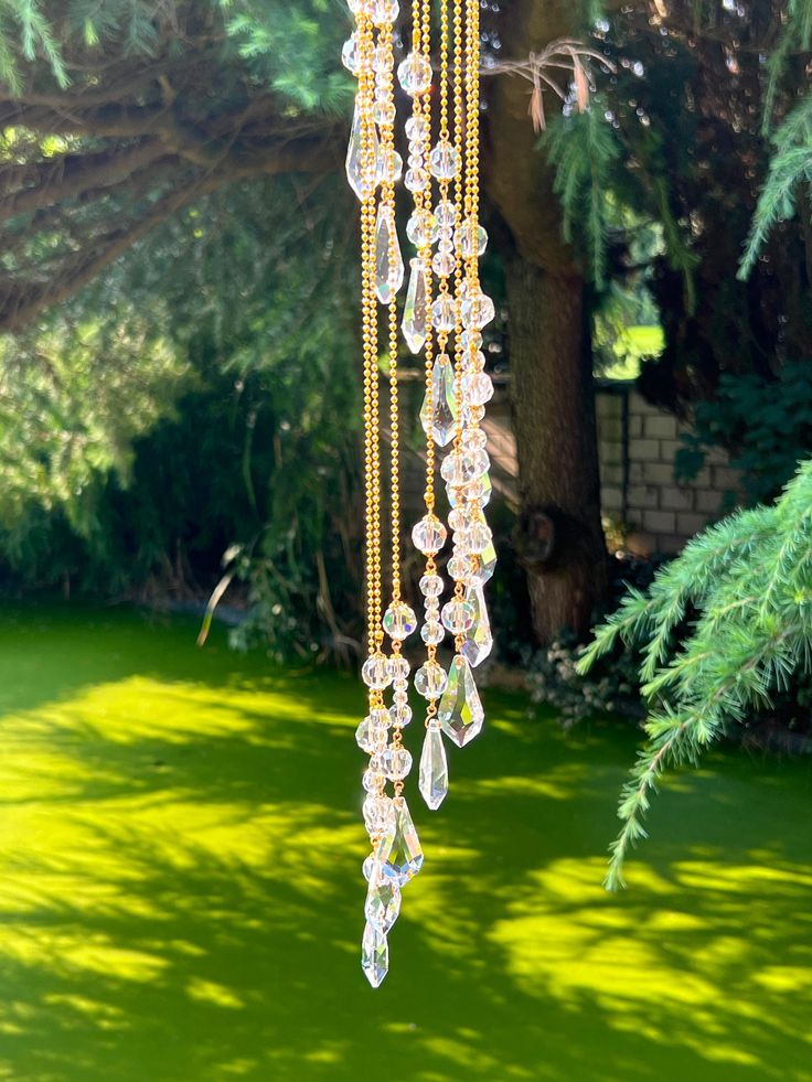 a group of glass beads hanging from a tree in a park or garden, with green grass and trees in the background