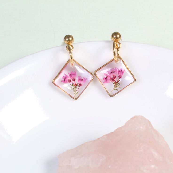 These dainty, handmade resin pressed flower earrings feature real pink heather flowers in a gold or silver diamond-oriented square setting. Real flowers are carefully preserved, clipped, then cured in several layers of resin. Small and lightweight, classy enough for a wildflower wedding, but tasteful enough that they're perfect for everyday wear.  Dimensions: From stud to bottom of earring - 1 inch Width - just over a 1/2 inch Ball studs are hypoallergenic and each pair comes with a steel and si Dainty Pink Gold Flower Jewelry, Elegant Pressed Flower Drop Earrings, Botanical Jewelry With Pressed Flowers, Gold Drop Earrings With Pressed Flowers, Rose Gold Pressed Flower Earrings, Dainty Handmade Rectangular Jewelry, Handmade Dainty Rectangular Jewelry, Rose Gold Pressed Flower Drop Earrings, Delicate Pressed Flower Jewelry