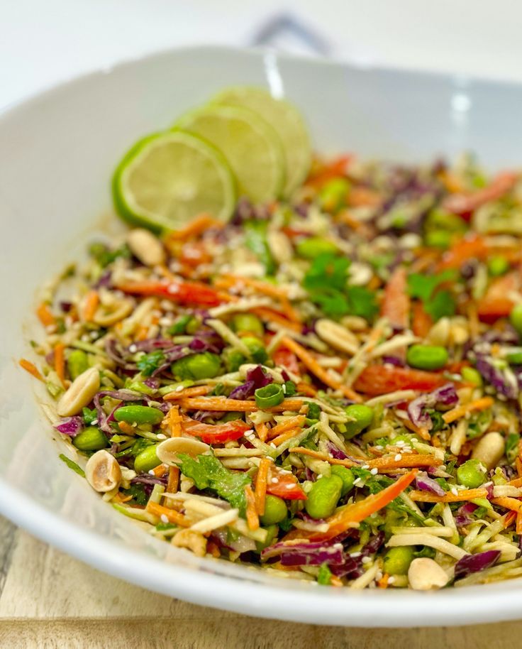 a salad in a white bowl with lime wedges on the side and another garnish