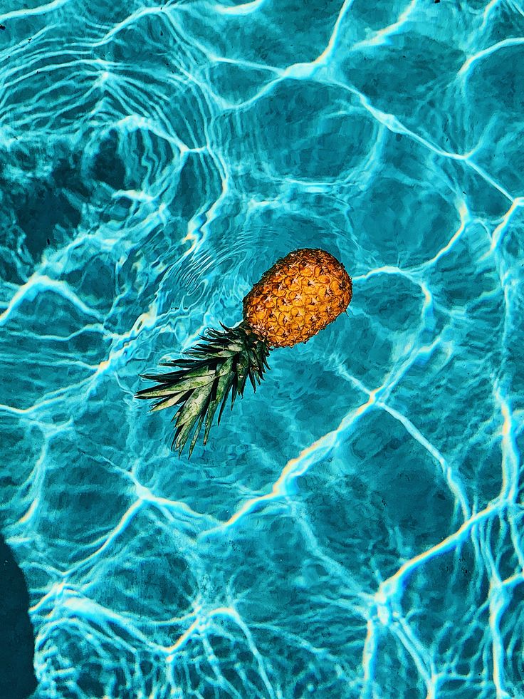 a pineapple floating on top of a blue pool with water ripples around it