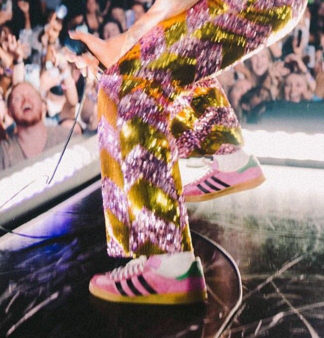 a person in colorful pants and sneakers on a stage with an audience behind them at a concert