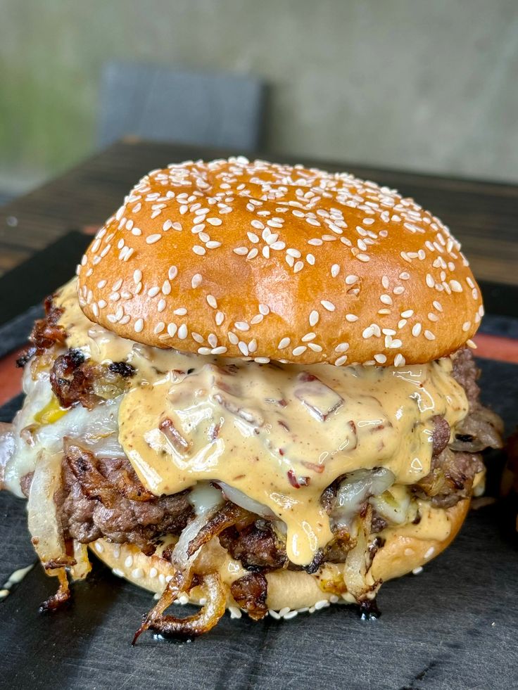 a cheeseburger with meat, onions and sauce on a black plate sitting on a wooden table