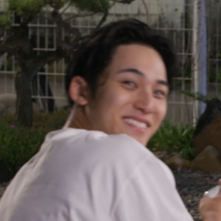 a young man is smiling and holding a cell phone in his hand while sitting on the ground