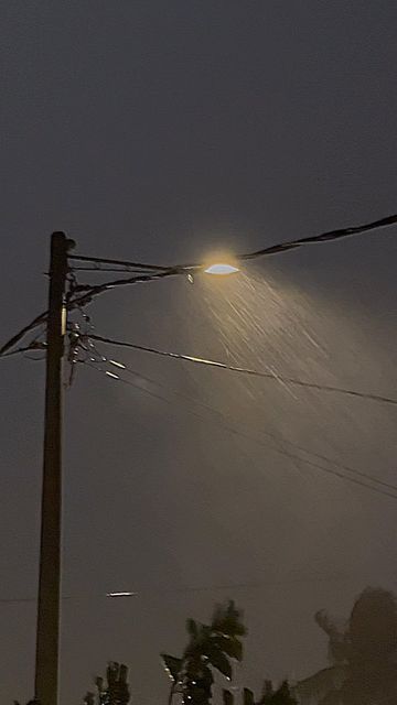 the street light shines brightly in the dark sky above some power lines and trees