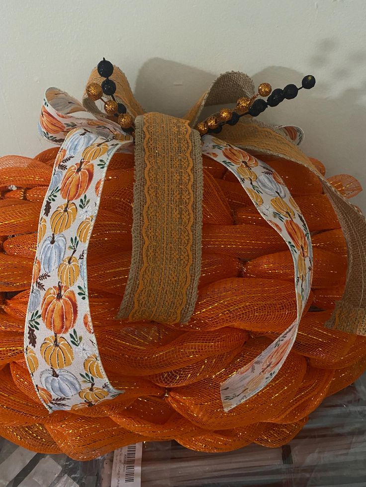 an orange wreath with ribbon and beaded decorations on the top, hanging from a wall