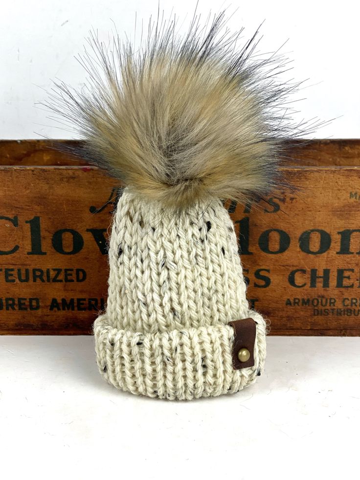 These are adorable little folded brim hats adorned with mini unstuffed faux fur poms.The hats measure 4" tall (not including the pom) x 3" Made from 100% wool yarn with suede tags, metal rivets and a suede tie for hanging.Listing is for 1 Mini Hat Ornament Adjustable Cozy Beige Hat, Cozy Adjustable Beige Hat, Adjustable Knitted Mini Hats For Winter, Brimmed Mini Hats In Beige For Winter, Cream Adjustable Crochet Hat For Winter, Adjustable Soft Knit Cream Hat, Adjustable Cream Soft Knit Hat, Winter Mini Hats With Short Brim Made Of Yarn, Winter Yarn Mini Hat With Short Brim