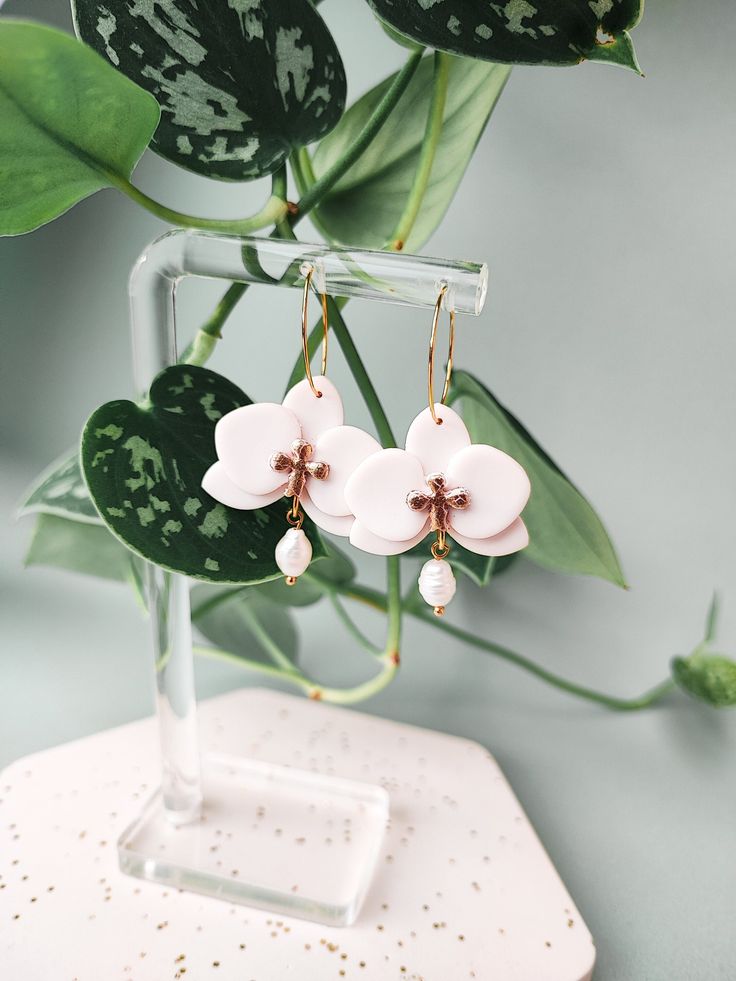 the pink flower earrings are on display next to a potted plant with green leaves