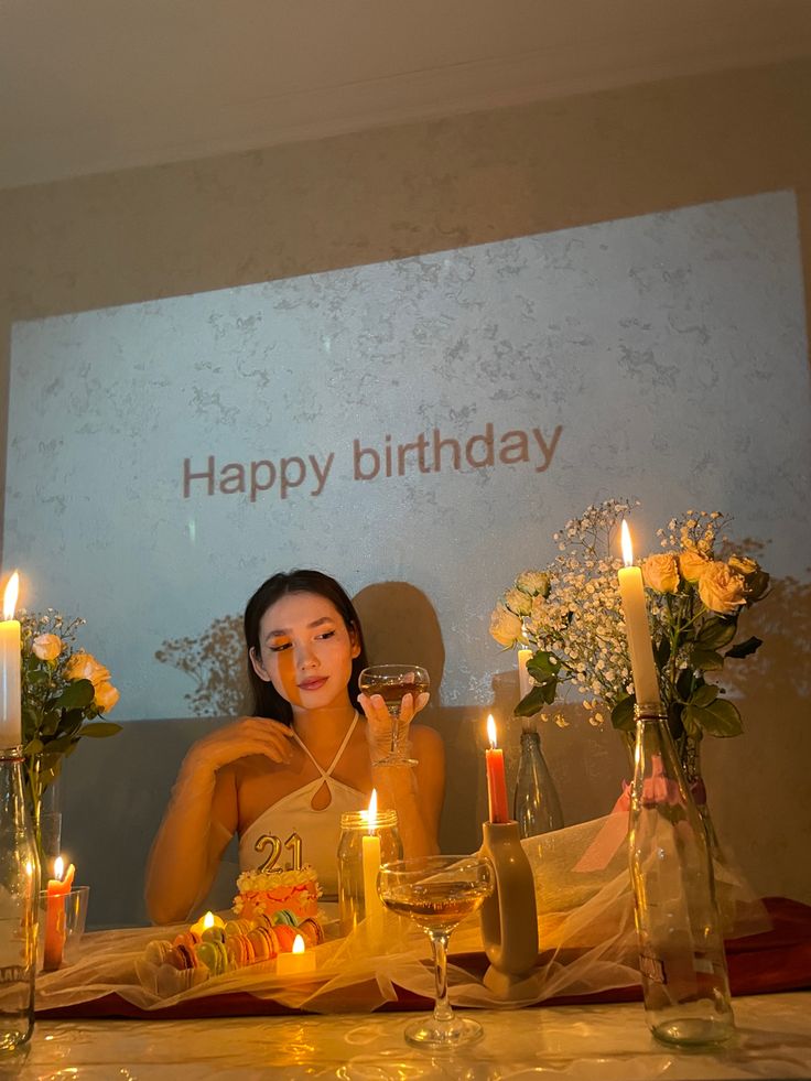 a woman sitting at a table with candles in front of her and flowers on the table