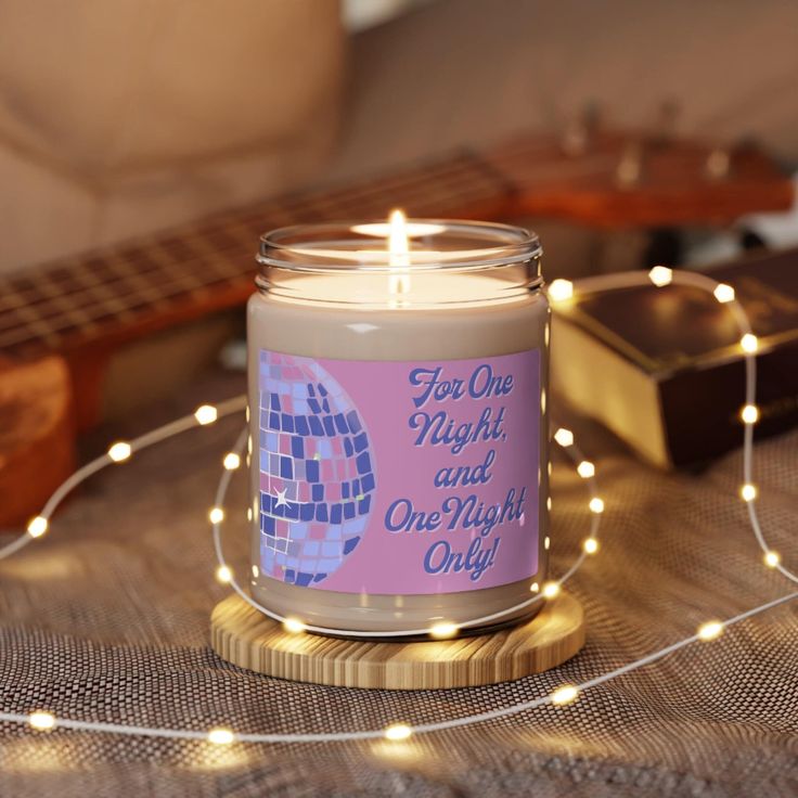 a lit candle sitting on top of a wooden table next to a string of lights